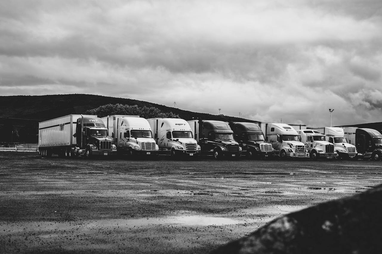 about-us Row of parked semi trucks in a rainy lot, captured in a dramatic black and white setting.